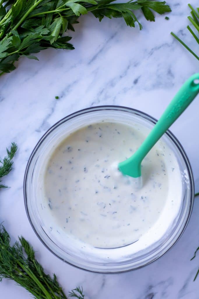 ranch dressing in a bowl with a green spoon on a marble table