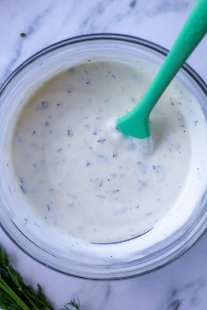 ranch dressing in a bowl with a green spoon on a marble table