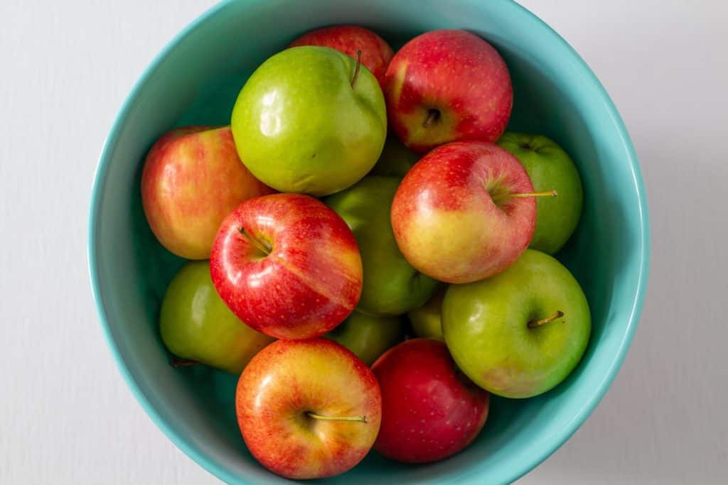 red and green apples in a bowl on a white background