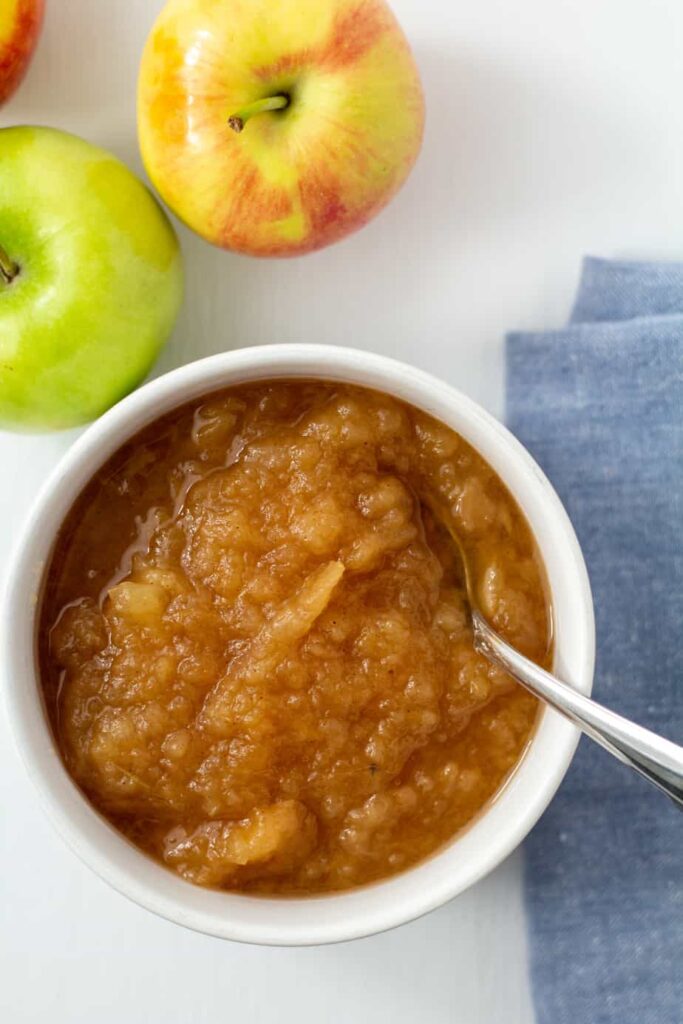 applesauce in a white bowl with a blue napkin and apples on the side