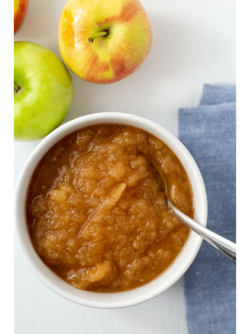 applesauce in a white bowl with a blue napkin and apples on the side