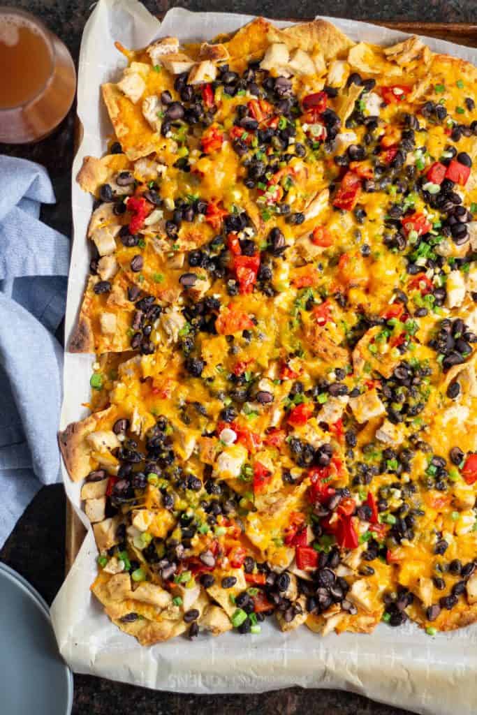 chicken nachos next to a blue napkin, plates, and a beer