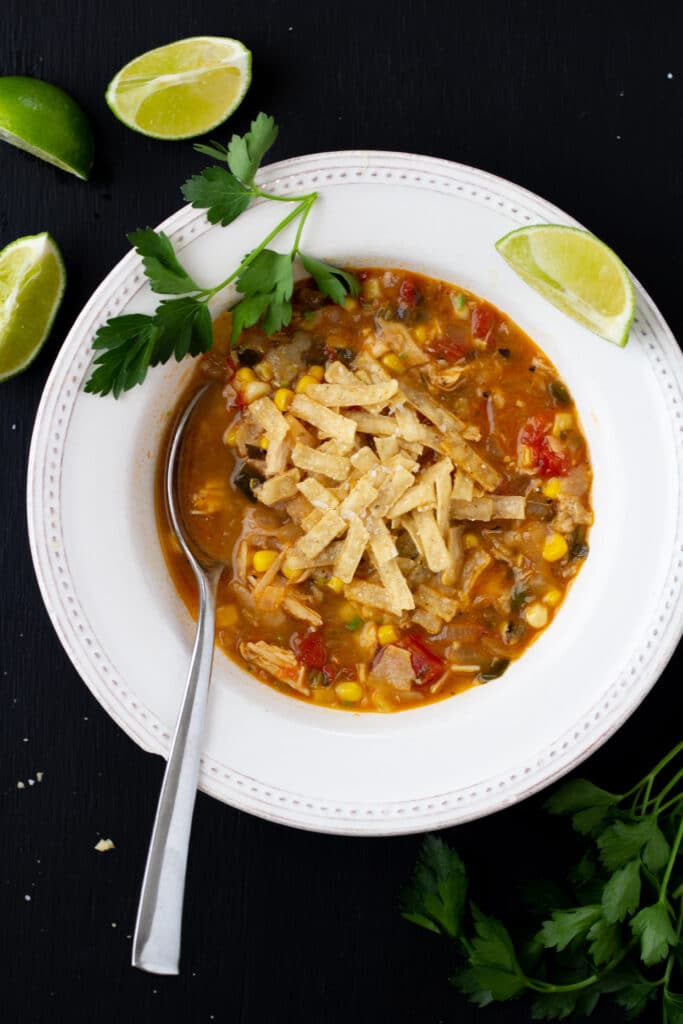 chicken tortilla soup in a white bowl on a black background with a spoon