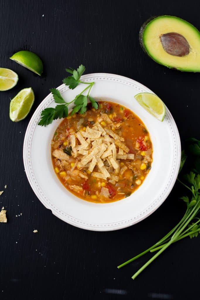 chicken tortilla soup in a white bowl on a black background with a spoon