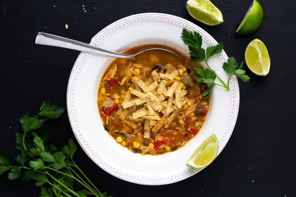 chicken tortilla soup in a white bowl on a black background with a spoon