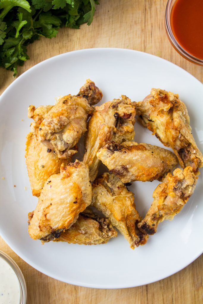 air fried chicken wings on a white plate with sauce on the sides