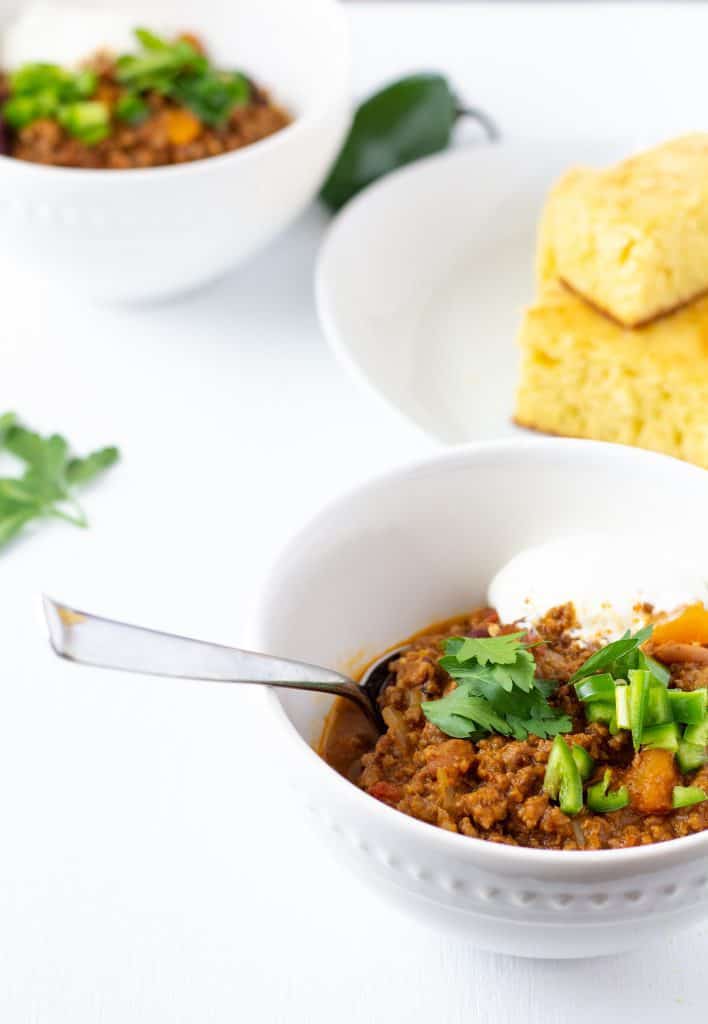 chili in a white bowl on a white background with a spoon. 