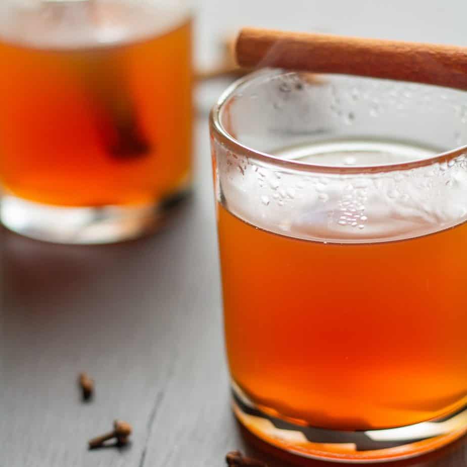 Apple cider in a clear glass on a black background with a cinnamon stick on top.