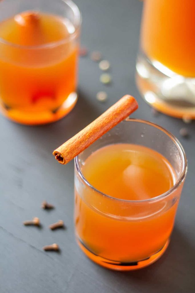 Apple cider in a clear glass on a black background with a cinnamon stick on top.