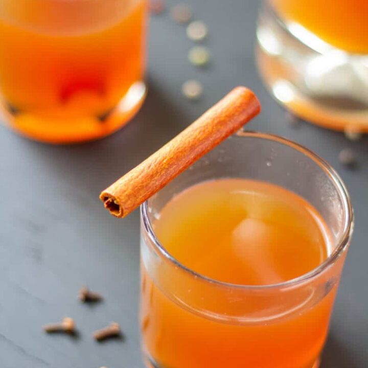 Apple cider in a clear glass on a black background with a cinnamon stick on top.