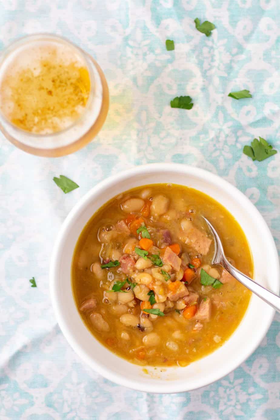 ham and bean soup in a white bowl with a glass of beer to the side