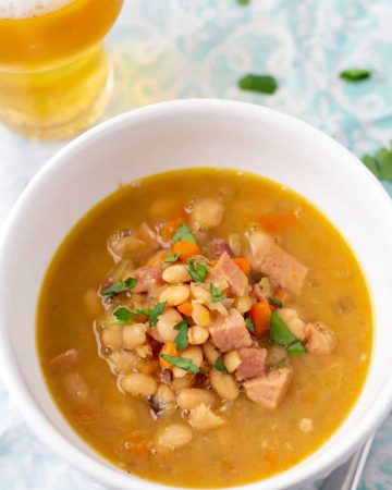 ham and bean soup in a white bowl with a glass of beer to the side