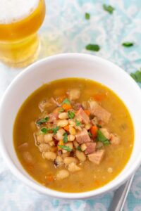 ham and bean soup in a white bowl with a glass of beer to the side