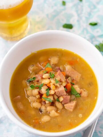 ham and bean soup in a white bowl with a glass of beer to the side