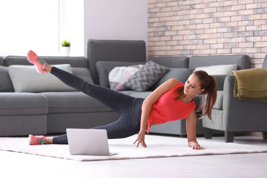 A woman exercising on the floor with a computer while spending time at home 