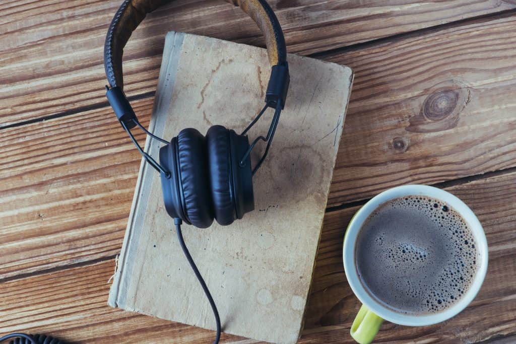 headphones on a book with a cup of coffee sitting on a wooden table