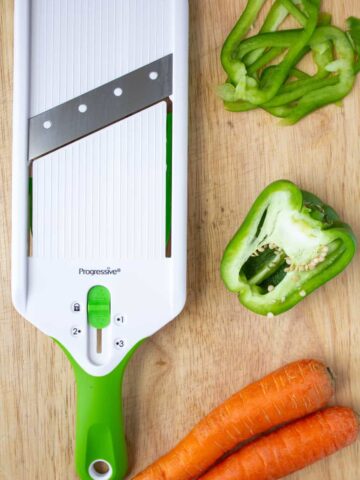 mandoline, green peppers, and carrots on a cutting board