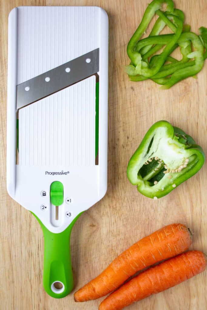 mandoline, green peppers, and carrots on a cutting board 