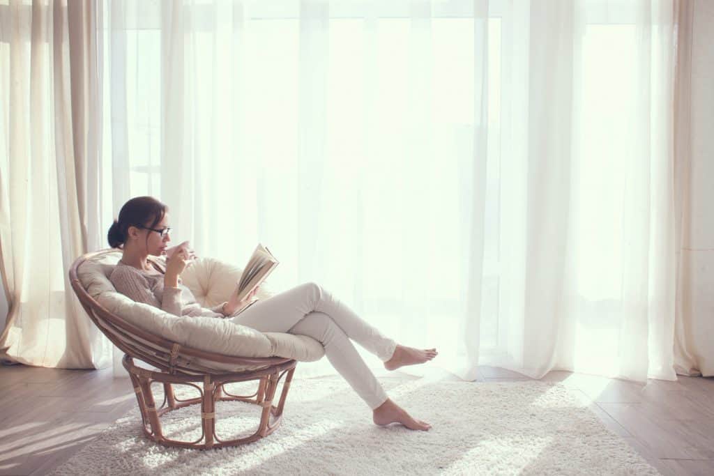 a woman reading in a white cushion chair while spending time at home 