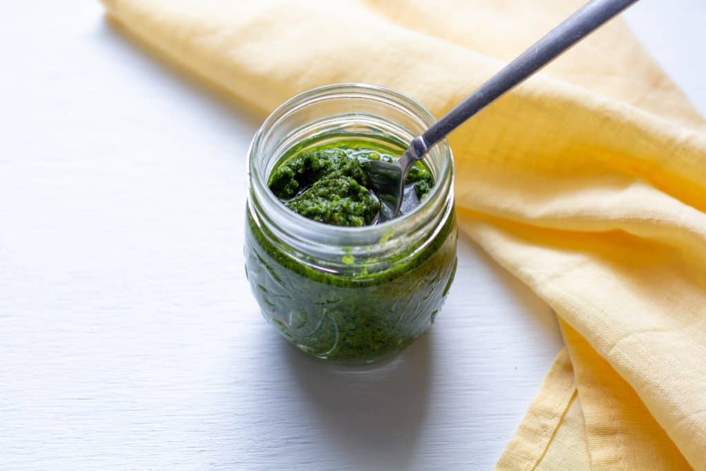 pesto in a jar on a white background with a spoon