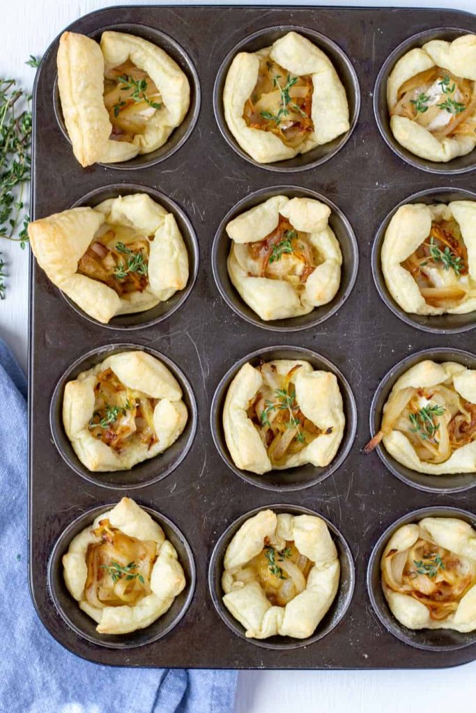 onion and brie appetizer bites in a muffin pan on a white background