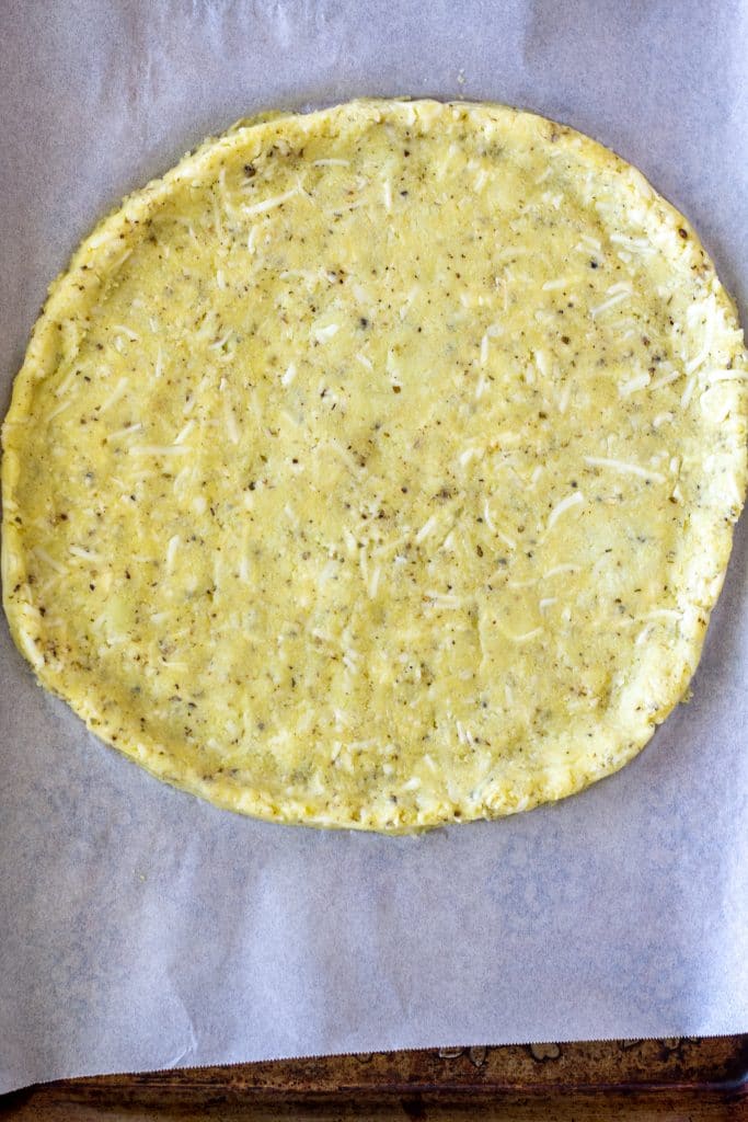 cauliflower pizza crust uncooked on parchment paper