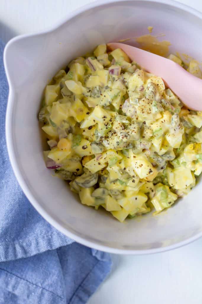 egg salad in a white bowl with a blue napkin and a pink spatula