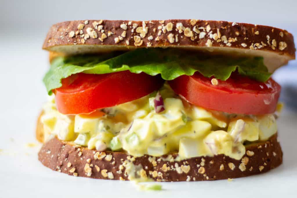 egg salad sandwich with lettuce and tomatoes on a white background