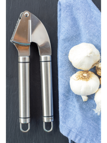 Garlic Press on a black background with garlic heads on the side sitting on a blue napkin