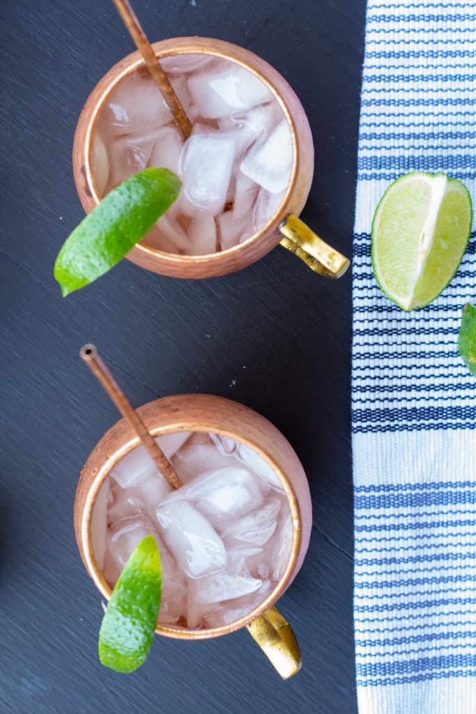 moscow mules in copper mugs on a black background with a white and blue striped napkin and sliced limes