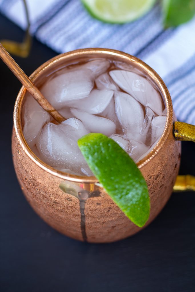 moscow mules in copper mugs on a black background with a white and blue striped napkin and sliced limes