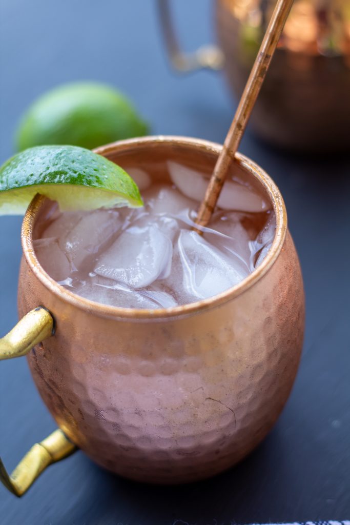 moscow mules in copper mugs on a black background with a white and blue striped napkin and sliced limes