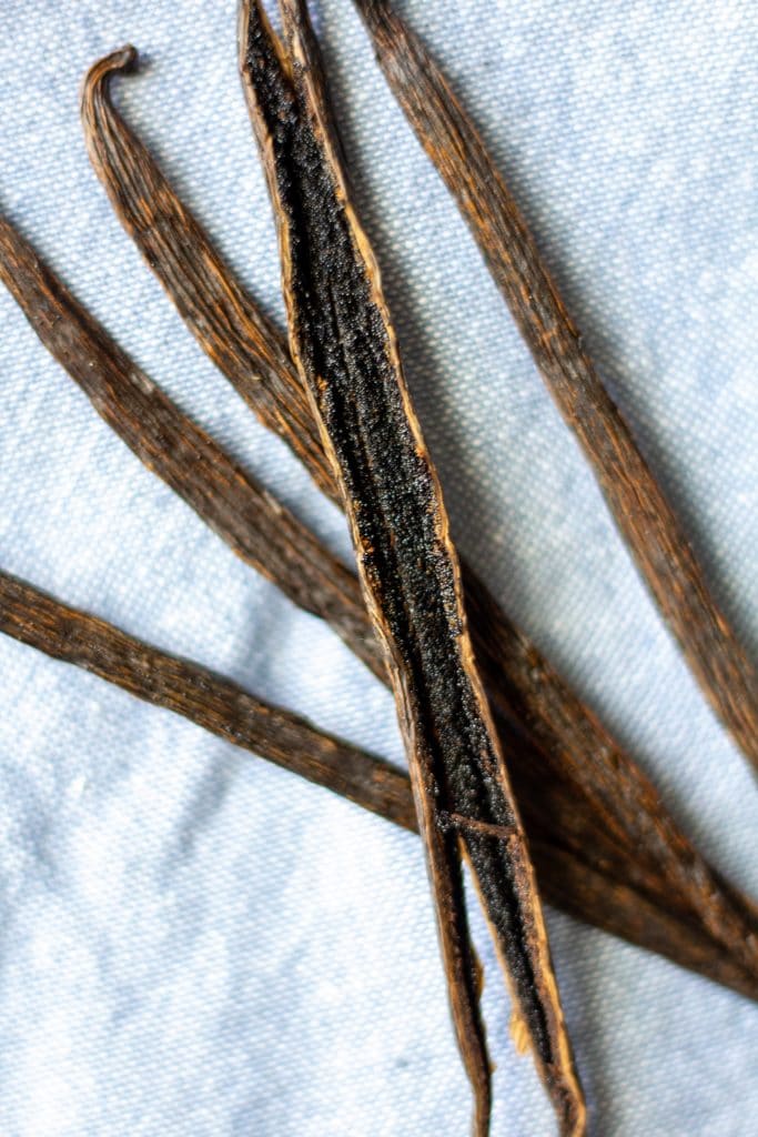 vanilla beans with one split open laying on a blue napkin