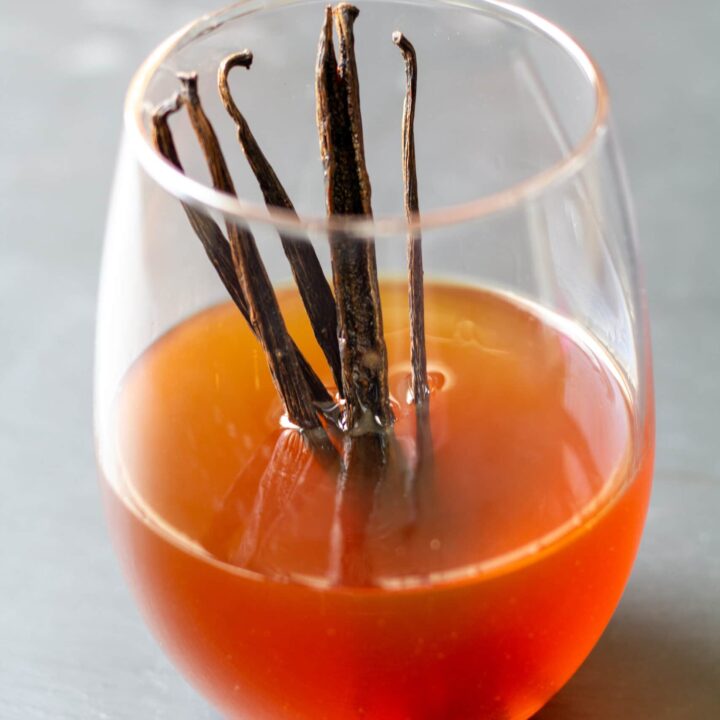 vanilla extract in a clear glass with vanilla beans standing up