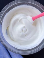 whipped cream in a glass bowl with a pink spoon on a black background