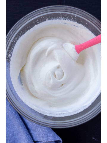 whipped cream in a glass bowl with a pink spoon on a black background