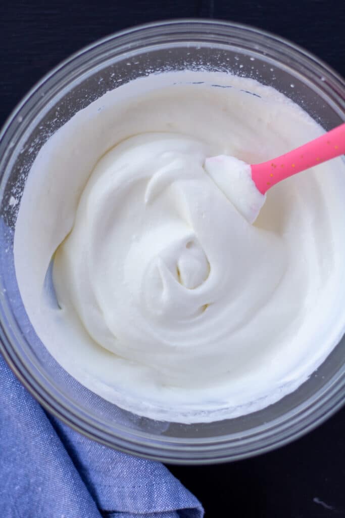 whipped cream in a glass bowl with a pink spoon on a black background