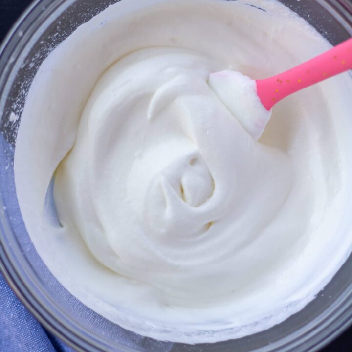 whipped cream in a glass bowl with a pink spoon on a black background