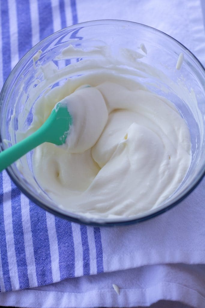 soft peaks whipped cream in a glass bowl with a green spoon on a white and blue background