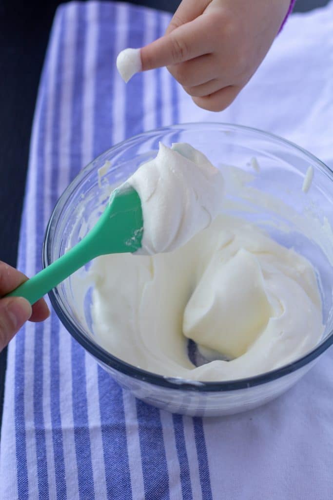 medium peaks whipped cream in a glass bowl with a green spoon on a white and blue background