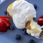 Whipped cream on a piece of cheesecake sitting on a blue plate with berries surrounding it