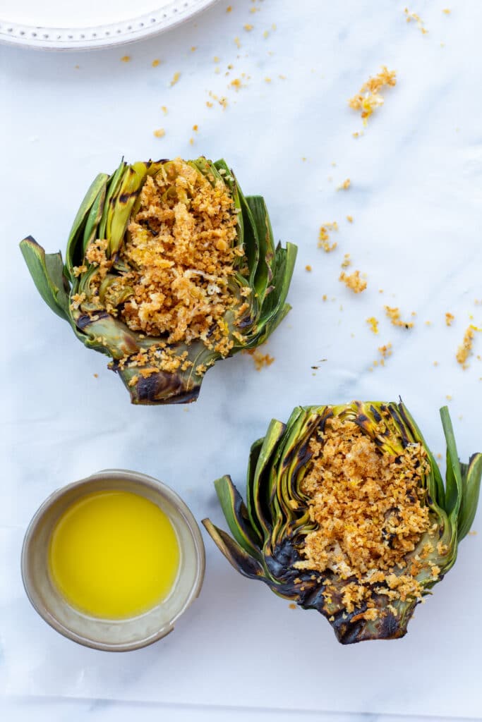 artichokes topped with a parmesan panko breading next to a side of butter on a white background