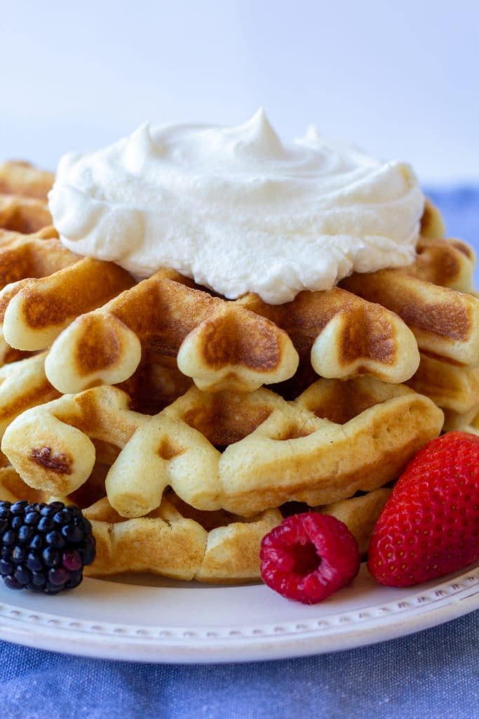 a close up of a stack of waffles topped with whipped cream with berries on the side