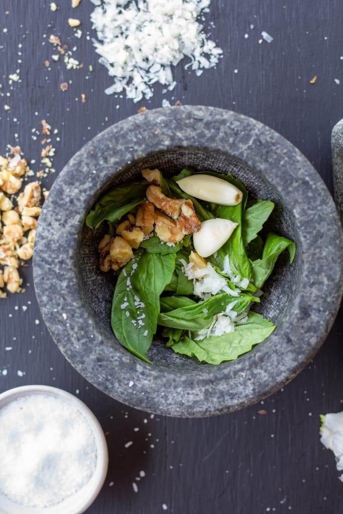 walnuts, garlic, salt, parmesan, and basil in a mortar on a black background