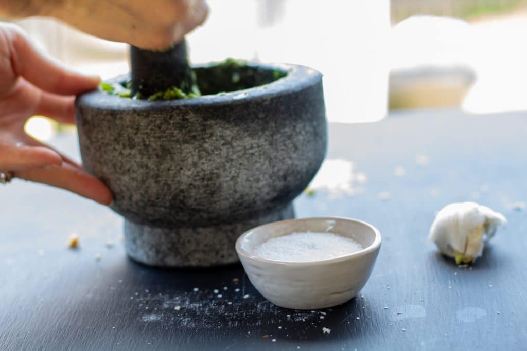 hands mixing with a mortar and pestle on a black background and a bowl of salt on the side