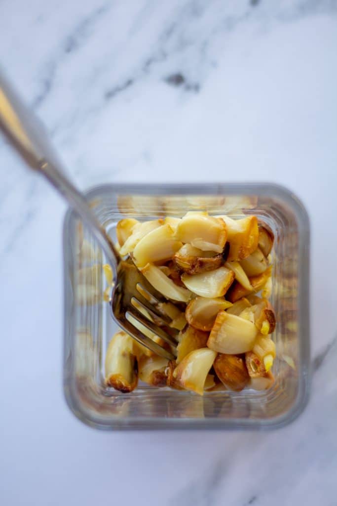 whole cloves of roasted garlic in a glass jar with a fork