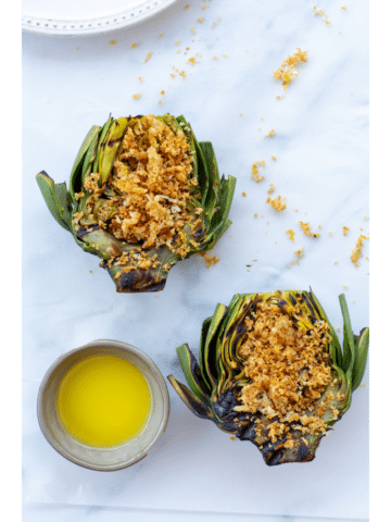 artichokes topped with a parmesan panko breading next to a side of butter on a white background