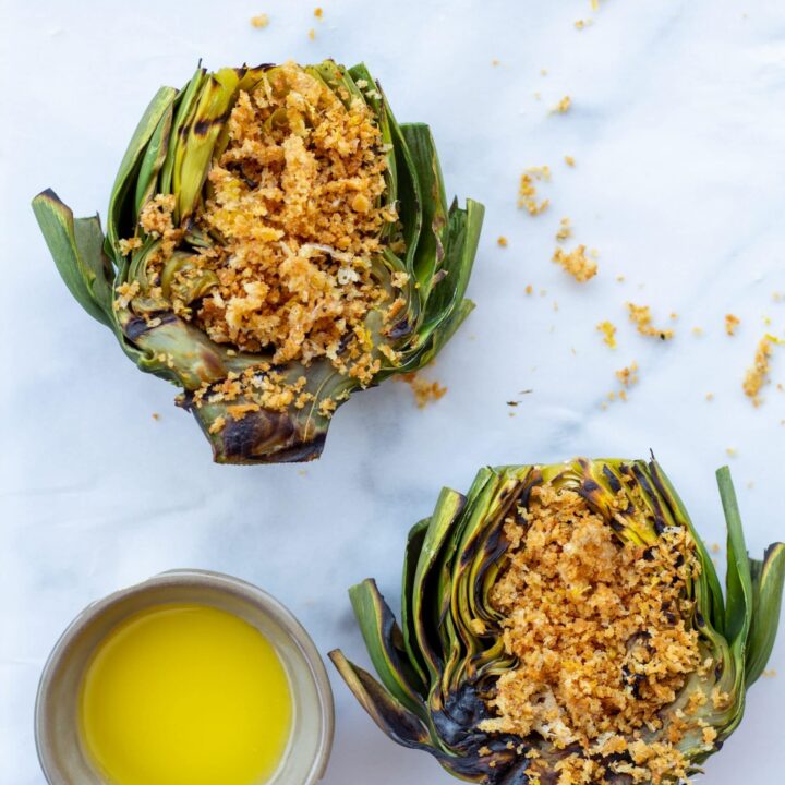 artichokes topped with a parmesan panko breading next to a side of butter on a white background