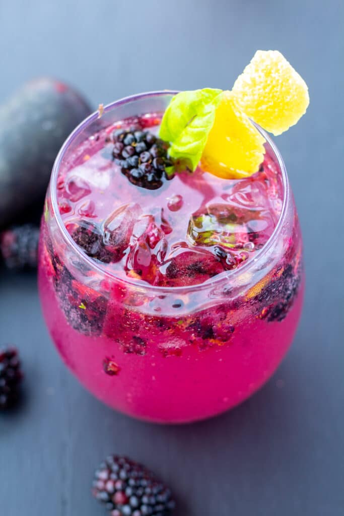 blackberry fizz in a clear glass with whole berries in and around the glass on a black background