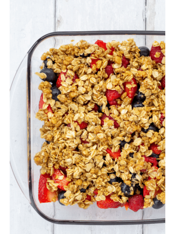 fruit in a glass pan with oat topping on a white background